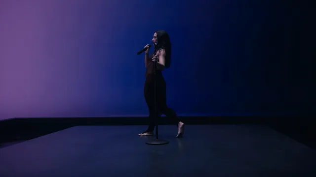 Demi Lovato singing barefoot in a blue-lit studio setting.