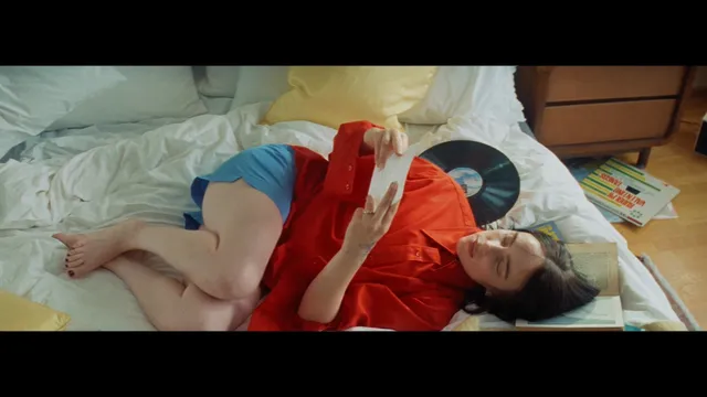 Billie Eilish a red-shirt screen scene while reclining on a bed.