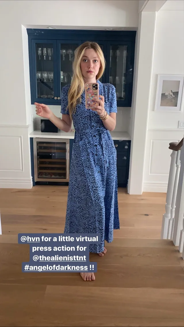 Dakota Fanning standing indoors in a blue dress for a mirror photograph.