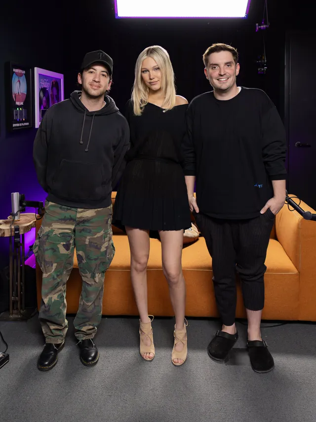 Grace VanderWaal standing between two people in a black dress and pale heels.