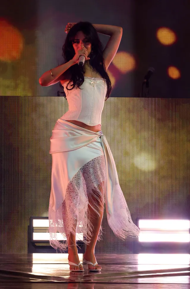 Camila Cabello singing onstage in a pale outfit and heels.