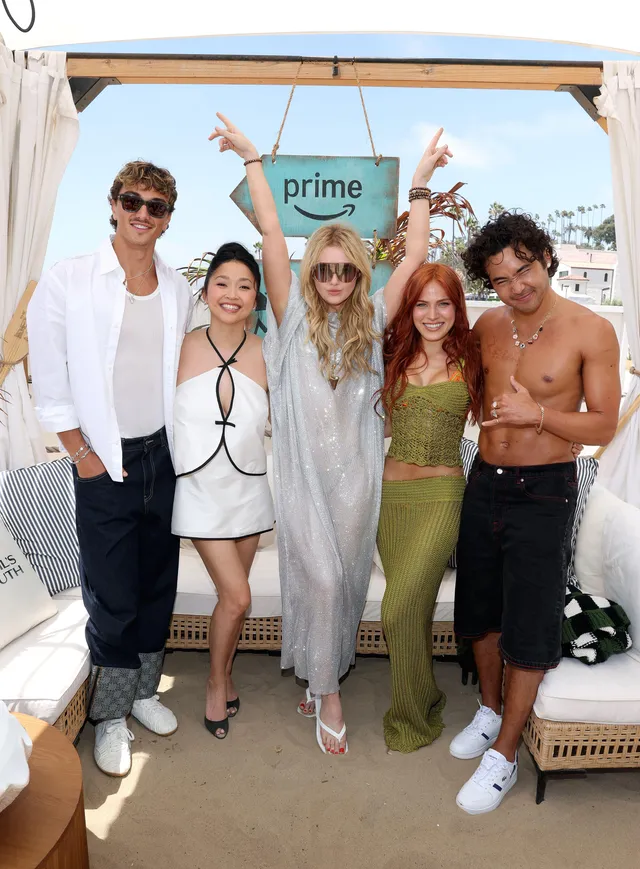Kathryn Newton posing with a group outdoors in a silver dress and heeled sandals.