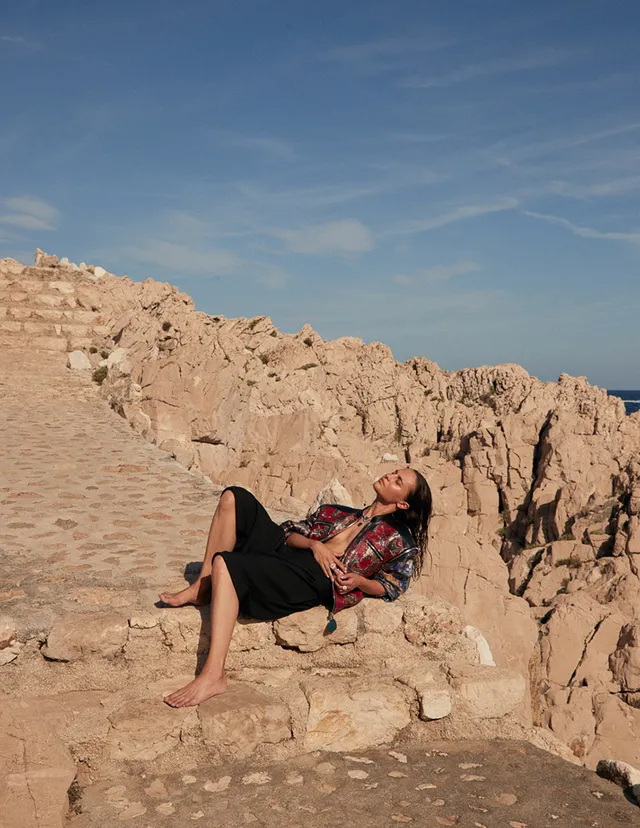 Alicia Vikander reclining on rocks in a fashion photograph.