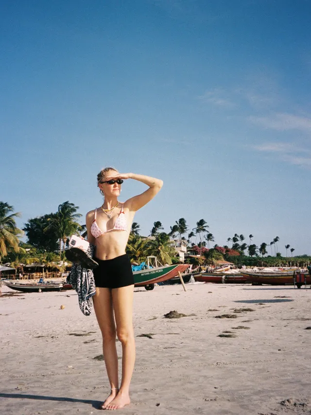 Maika Monroe standing barefoot on a beach.