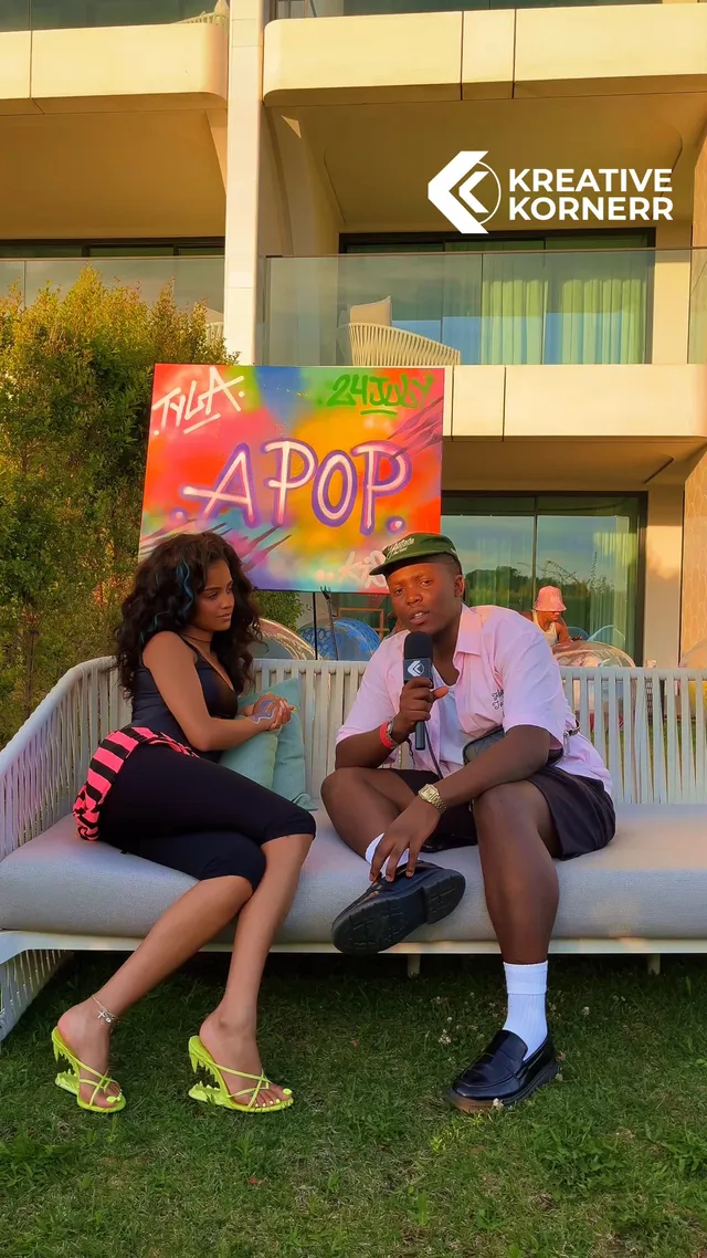 Tyla sitting in bright heeled sandals beside an interviewer outdoors.