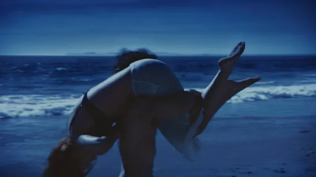 Mackenzie Ziegler posing on beach sand with a bare sole raised in a dark scene.