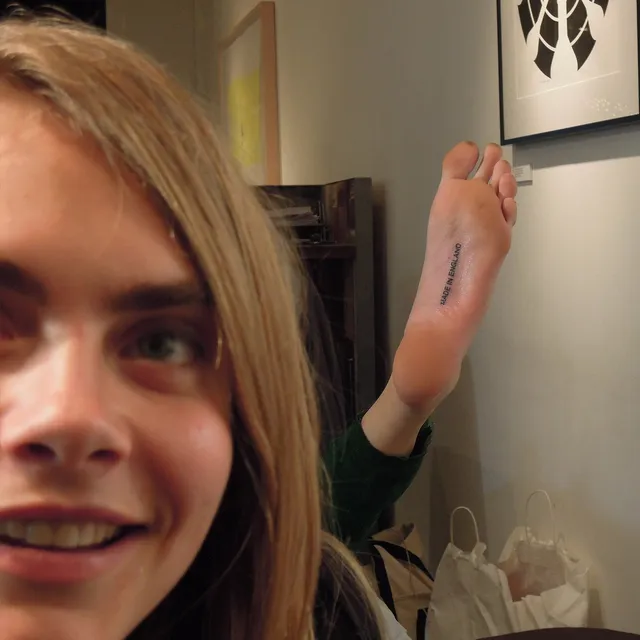 Cara Delevingne taking a playful photograph with one foot raised.