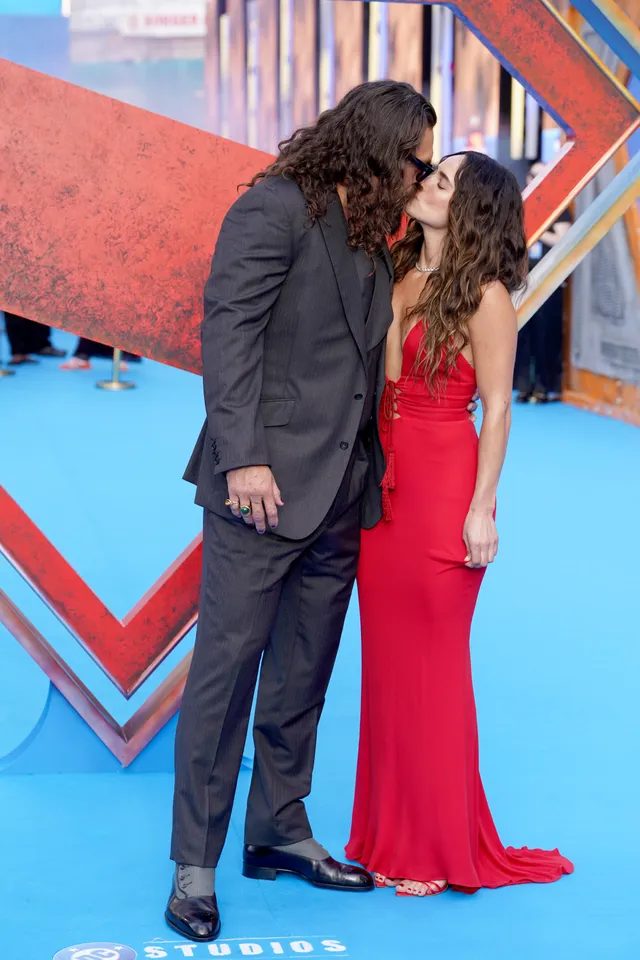 Adria Arjona posing beside a man in a long red gown at a premiere.