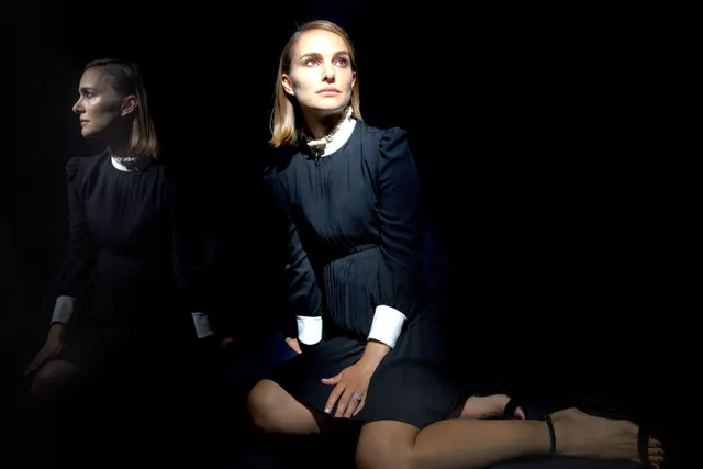 Natalie Portman sitting on a bench in a dark outfit.