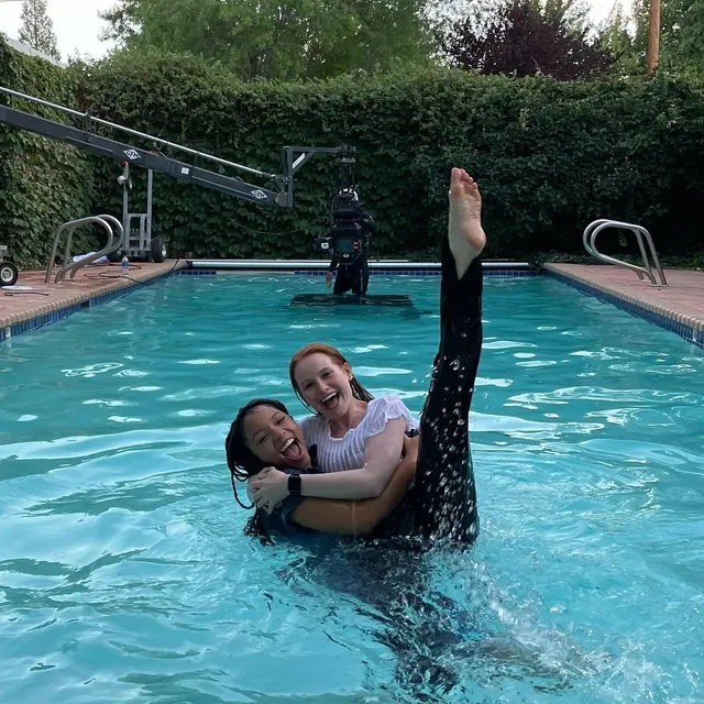 Madelaine Petsch posing with a companion in a pool with a bare foot raised.