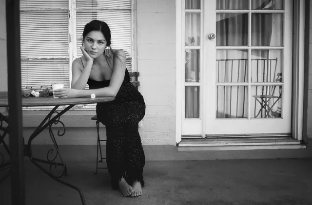 Olivia Rodrigo leaning on an outdoor table in a monochrome portrait.