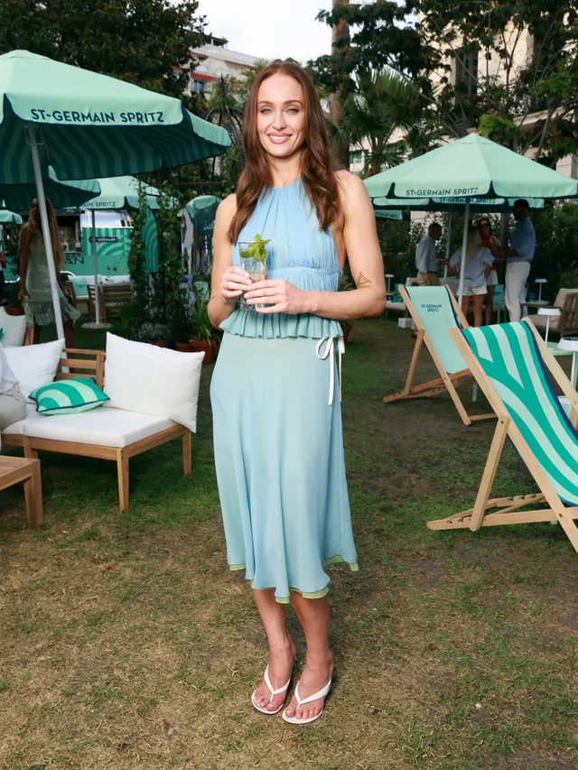 Sophie Turner a blue dress and white heels at an outdoor event.