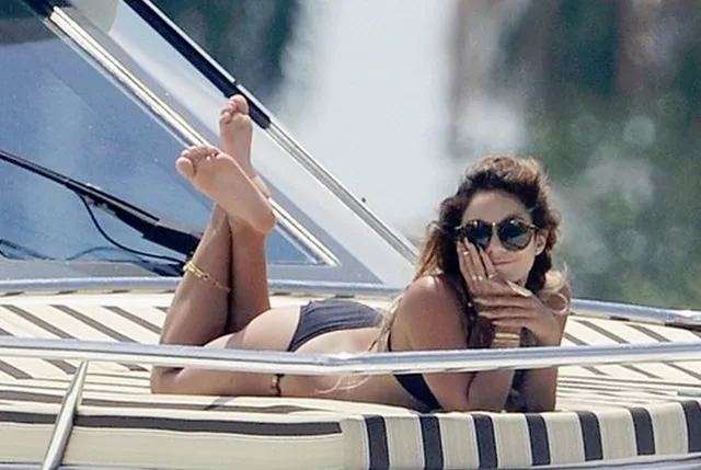 Vanessa Hudgens reclining in a black swimsuit with bare feet raised.