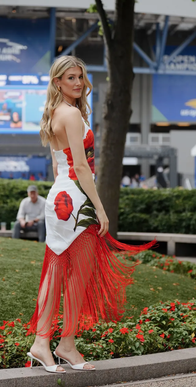 Eugenie Bouchard wearing pale heels and a red-and-white dress at a tennis venue.