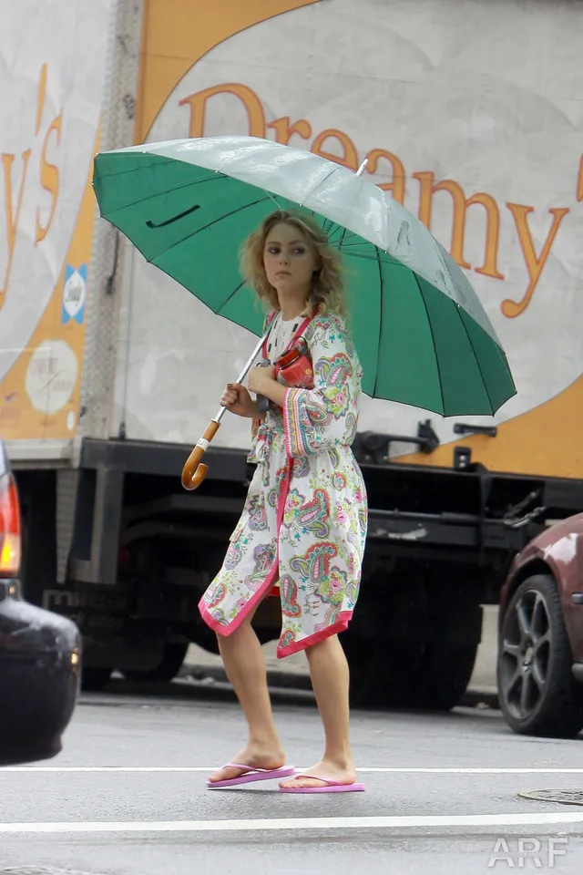 AnnaSophia Robb standing beside a vehicle beneath an umbrella.