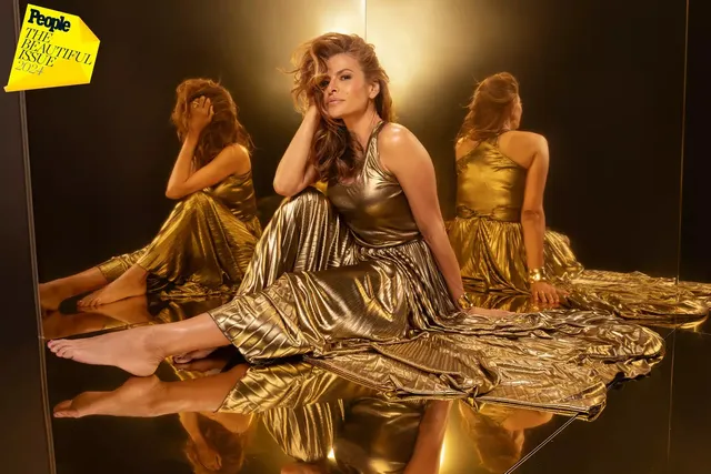 Eva Mendes sitting on a mirrored surface in a gold outfit.