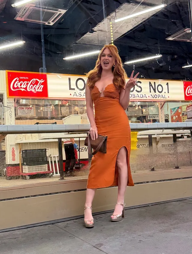 Isla Fisher posing outdoors in a long orange dress.