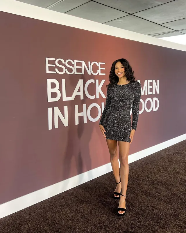 Greta Onieogou posing in a dark mini dress and black ankle-strap heels at an event.