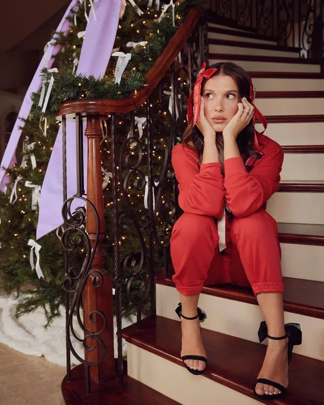 Millie Bobby Brown sitting on stairs in a red outfit.