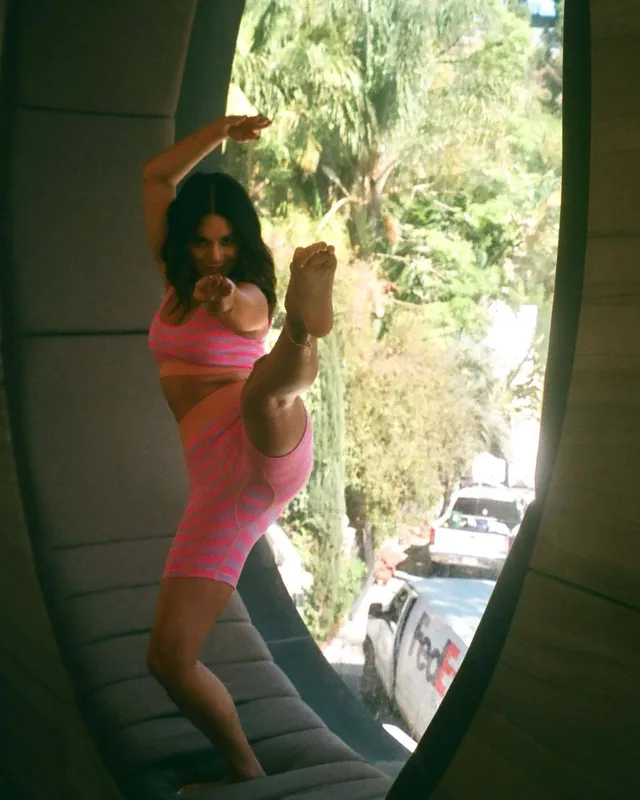 Vanessa Hudgens dancing barefoot in a pink outfit with one leg raised.
