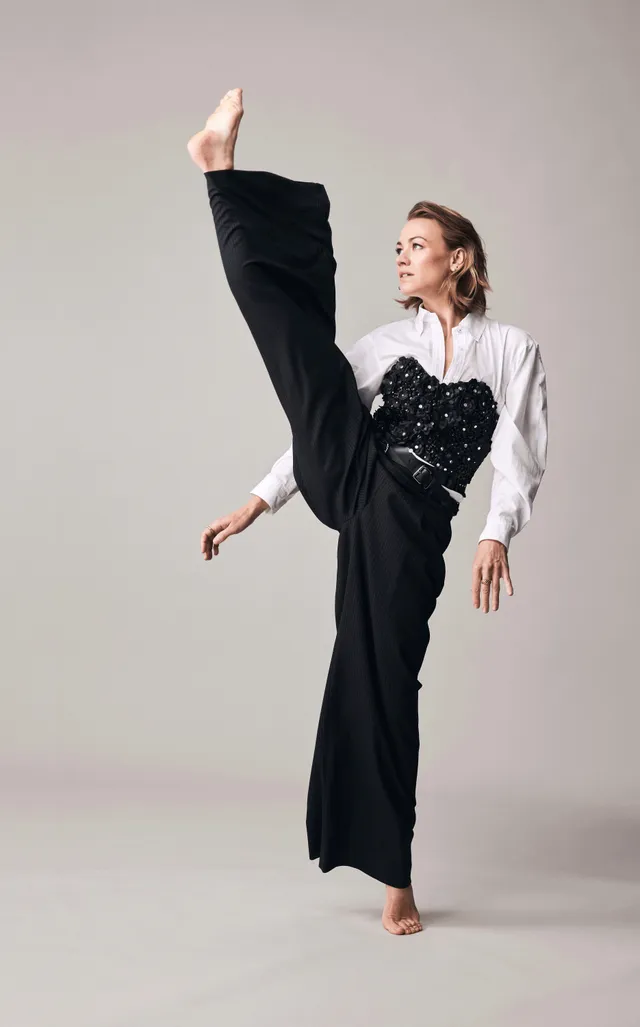 Yvonne Strahovski posing for a studio portrait in wide-leg trousers.