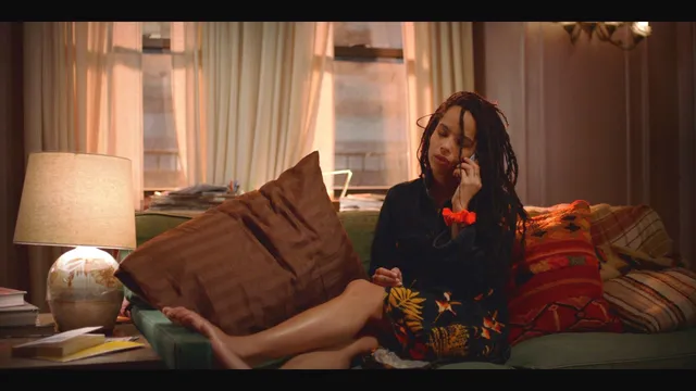 Zoë Kravitz resting her feet on a sofa in a screen scene.