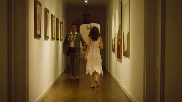 Odessa A'zion walking barefoot in a pale dress in a hallway scene.