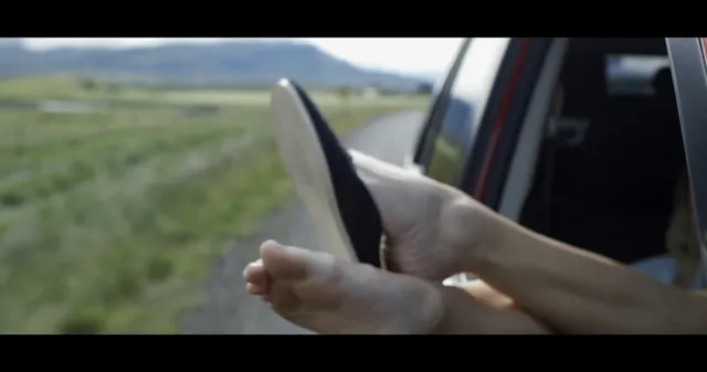 Maika Monroe resting a bare foot outside a vehicle window in a scene.