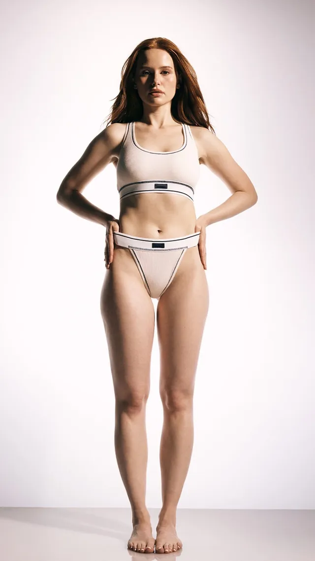 Madelaine Petsch posing barefoot in pale activewear against a white backdrop.