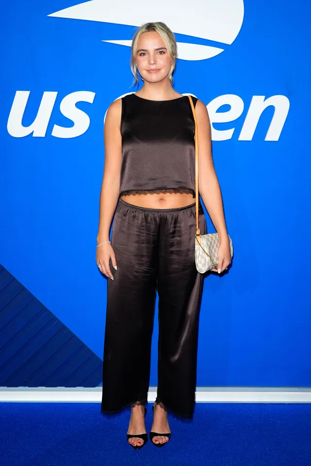 Bailee Madison wearing a dark satin outfit and black heels at the US Open.