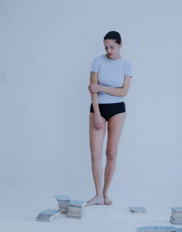 Adriana Lima standing barefoot in a pale top and dark shorts.