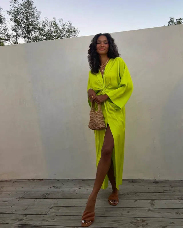 Greta Onieogou posing in a lime green robe-style dress and gold heels.
