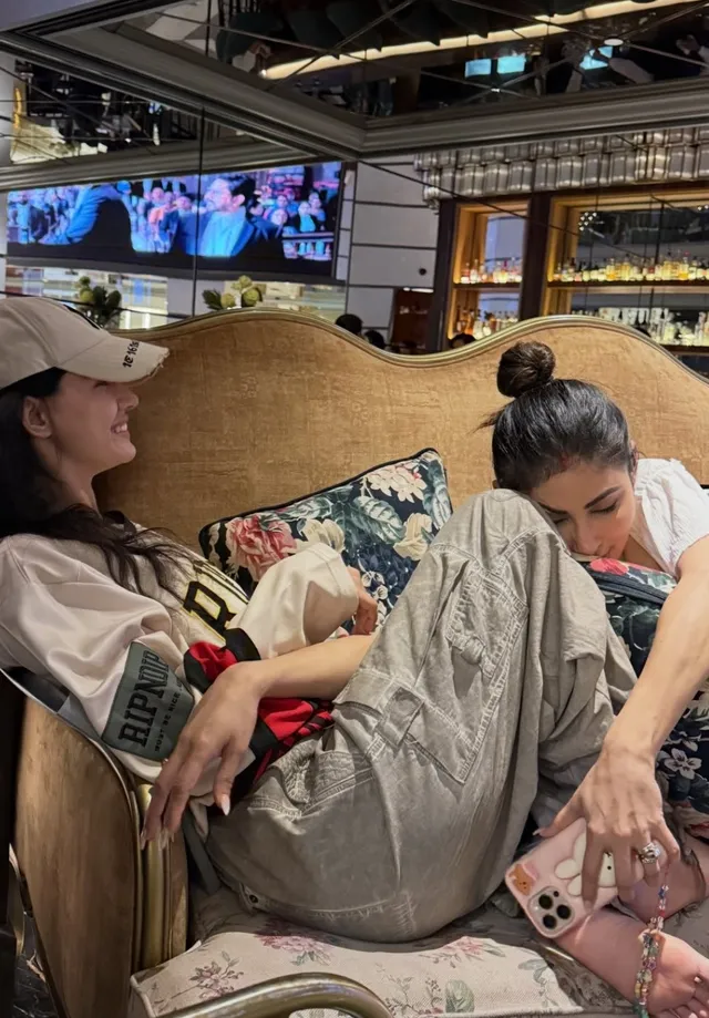 Disha Patani reclining barefoot on a sofa beside a companion.