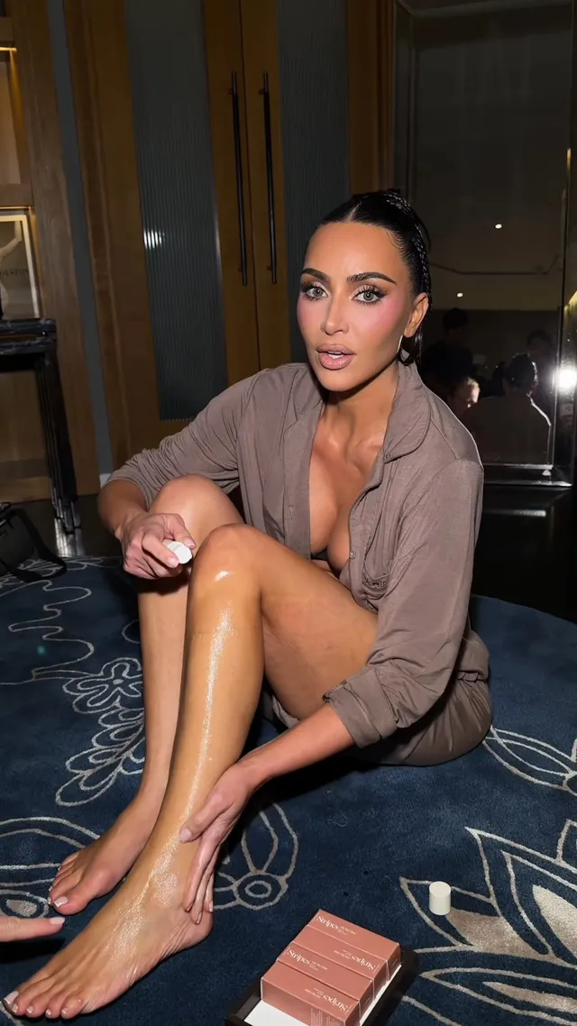 Kim Kardashian sitting on a carpet in a brown shirt.