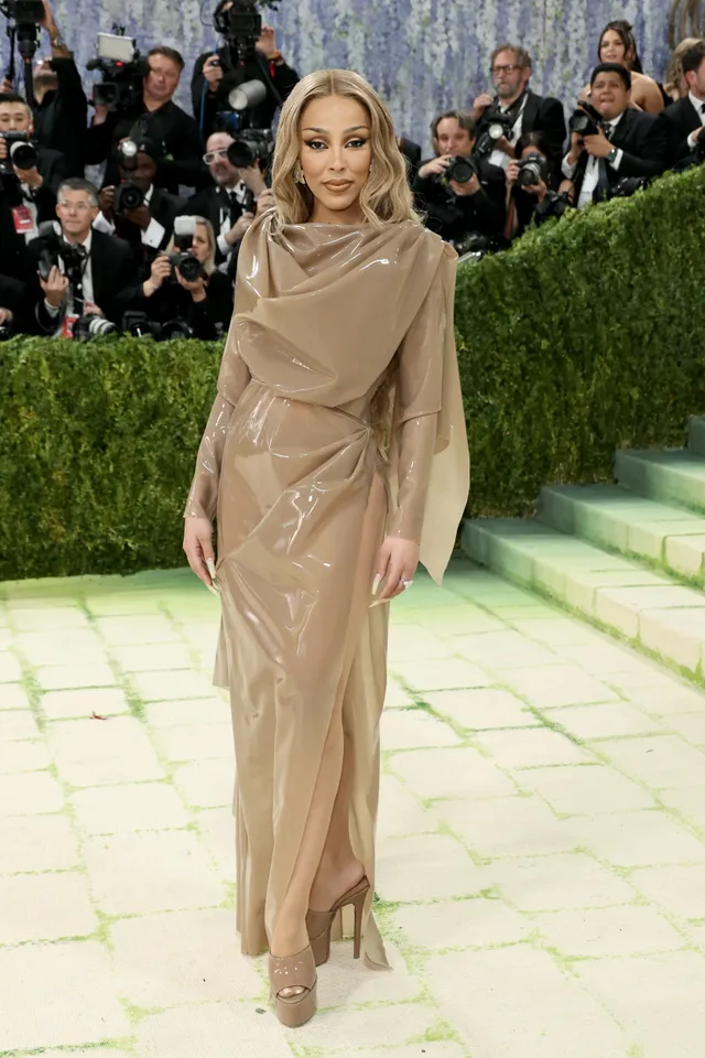 Doja Cat walking at an event in a tan outfit and platform heels.
