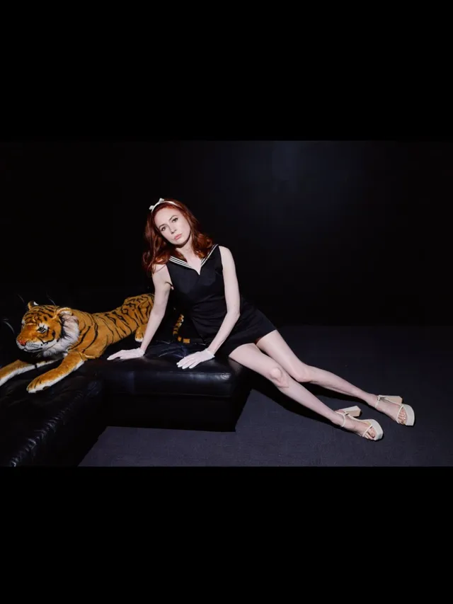Karen Gillan reclining barefoot beside a tiger prop in a studio.