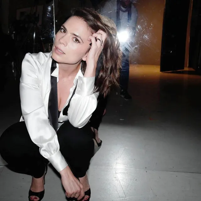 Hayley Atwell crouching in a white shirt and black pumps.