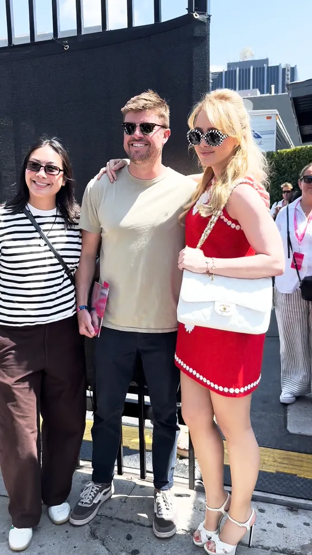 Kathryn Newton standing with two people in a red dress and pale heels.