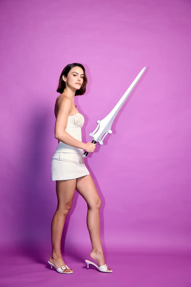 Camila Mendes posing with a prop sword in pale heels.