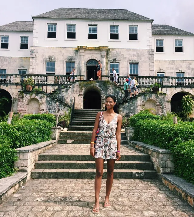 Greta Onieogou posing on stone steps in a floral outfit and flat sandals.