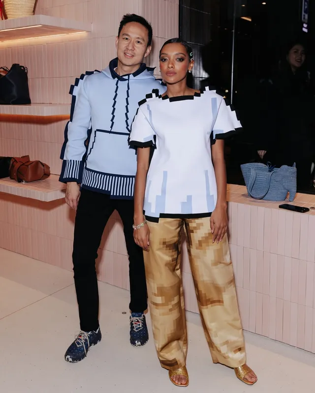 Sophie Wilde posing beside a man in gold trousers and heeled sandals.