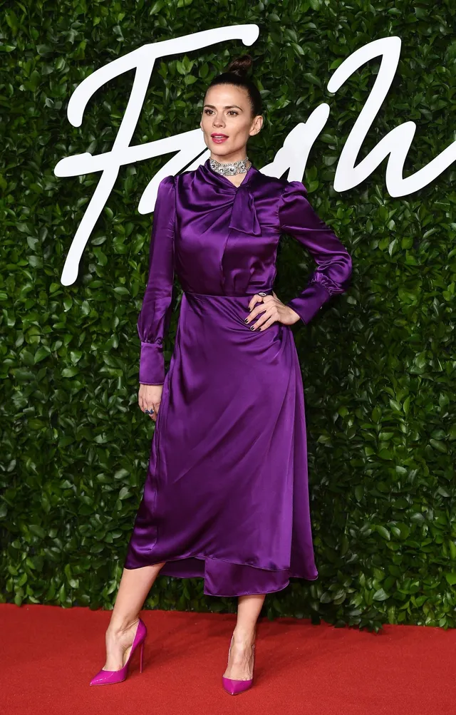 Hayley Atwell posing in a purple dress and bright pumps.