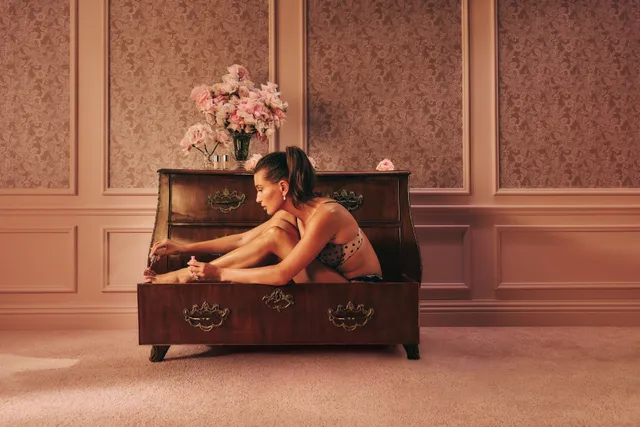Hailey Bieber sitting inside a trunk in a pink room.