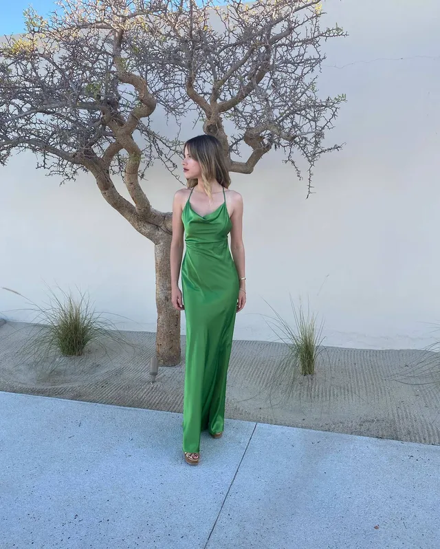 Halston Sage posing outdoors in a long green dress and heels.