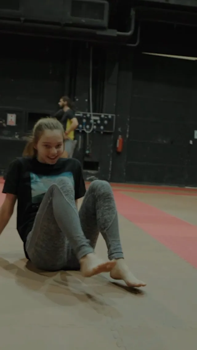Emma Myers sitting barefoot in gray leggings on a training mat.