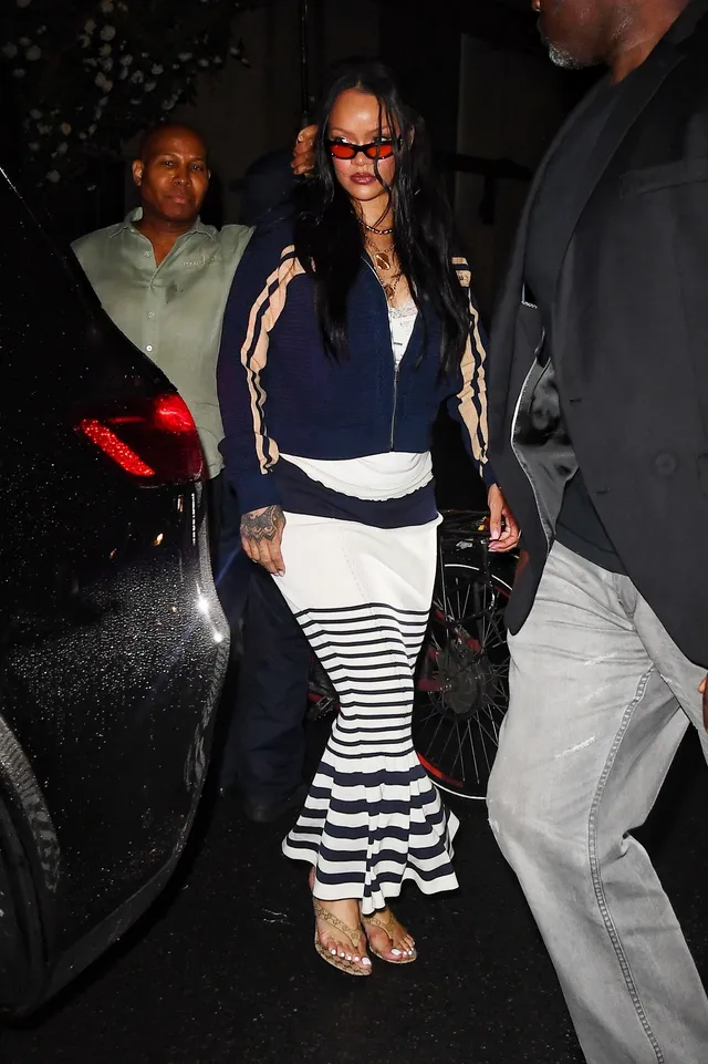 Rihanna walking at night in a striped skirt and gold sandals.