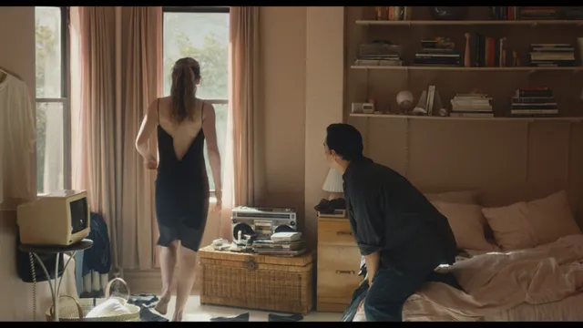 Sarah Pidgeon standing by a window in a black dress in a scene.
