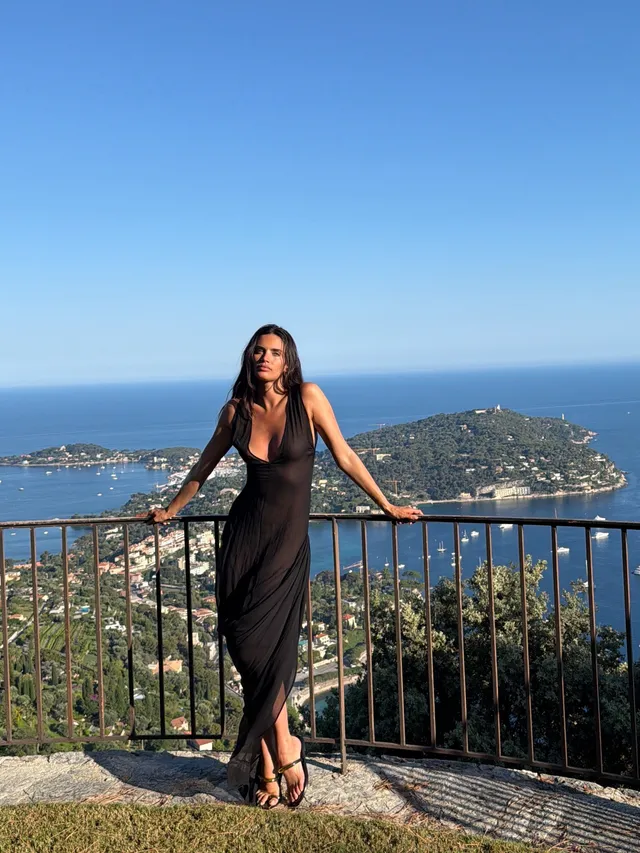 Sara Sampaio wearing flat sandals with a long black dress on a scenic terrace.