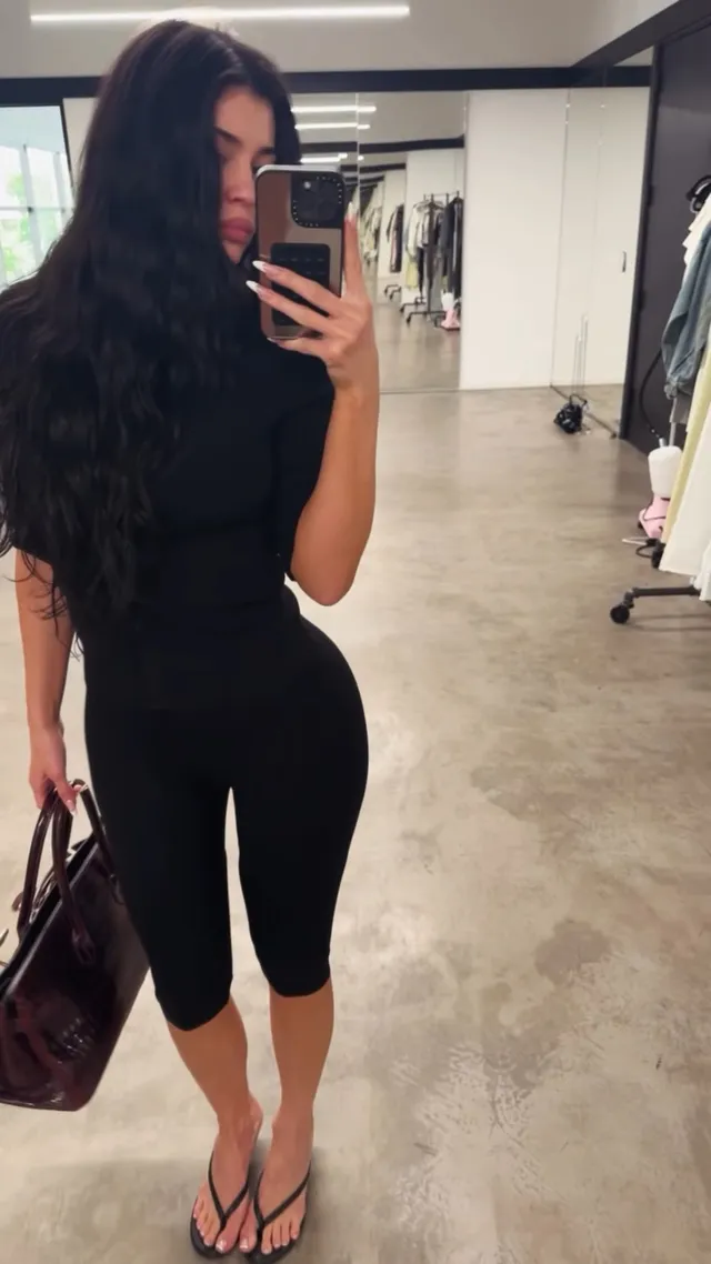 Kylie Jenner taking a mirror photo in black trousers and flip flops.