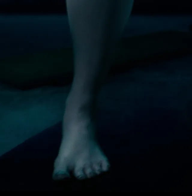 Monica Bellucci a close screen detail of bare feet in dim light.